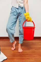 Woman in rubber gloves holding bucket and laptop on wooden floor