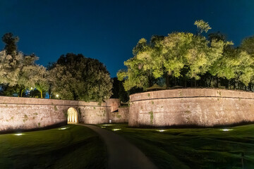 Night view of the historic walls of Lucca, Tuscany, Italy, beautifully lit with trees and a clear night sky.
