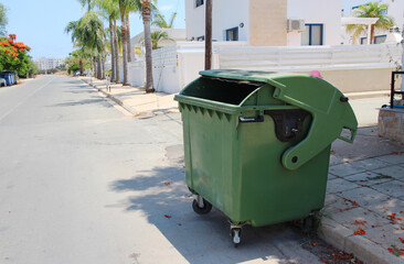 Green plastic trash container, trash can in the middle of the street. Reservoir for collecting, sorting and processing waste. Waste tank on a rotary on the street of Cyprus