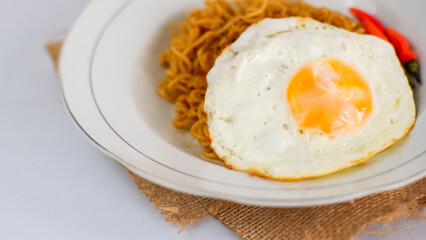 Fried noodles with fried egg and red cayenne pepper. Served on a serving white plate. Isolated on white background.