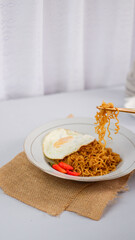 Fried noodles with fried egg and red cayenne pepper. Served on a serving white plate. Isolated on white background.