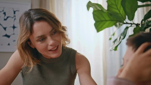 Smiling mother talking child at greenery living room closeup. Woman stroking son