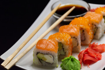 White plate with sushi and chopsticks beside soy sauce bowl