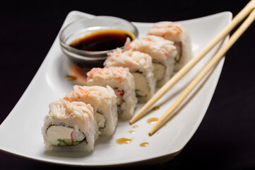 A plate of sushi with chopsticks and a bowl of soy sauce on a table