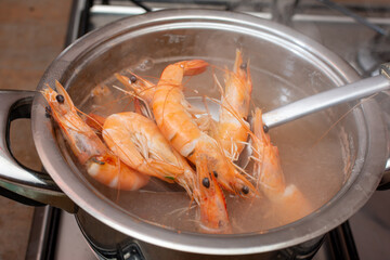 Shrimp are being cooked in a pot of boiling water with a spoon