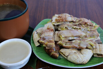 Smashed Grilled Banana topped with coconut milk and placed next to hot black coffee. on the brown wooden table

