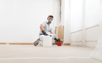 Man Worker Spraying Product on Wall to Remove Mold, Wearing Protective Gloves and a Respirator...