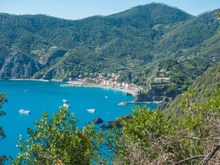 Naklejka premium Picturesque distant view of Monterosso al Mare with beach, ships and boats seen from Azure Trail to Vernazza with green cliffs, rock, clear blue sky and sea. National park Cinque Terre, Liguria, Italy