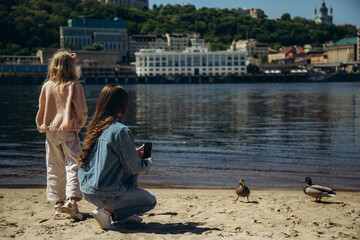 Mom and daughter take pictures of ducks on the bank of the city river.