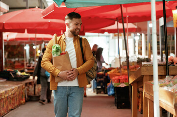 Smiling, holding shopping paper bag with products. Handsome man is on the street market or bazaar