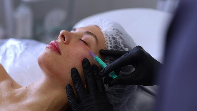 A professional beautician injects Botox into the face of a young woman