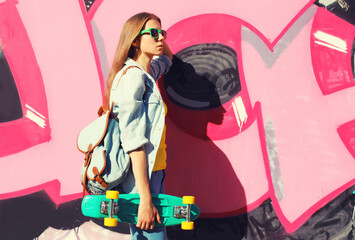 Stylish young girl with skateboard in glasses, modern teenager girl posing against the graffiti wall