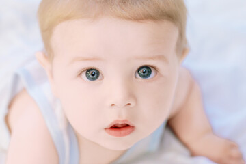 Adorable baby boy lying on stomach and looking with big blue eye