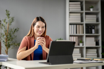 A woman is sitting at a desk with a laptop and a cup of coffee