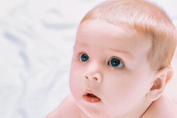 Cute baby boy lying on stomach and looking up with big blue eyes