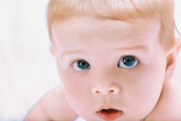 Cute baby with blue eyes lying on bed and looking up