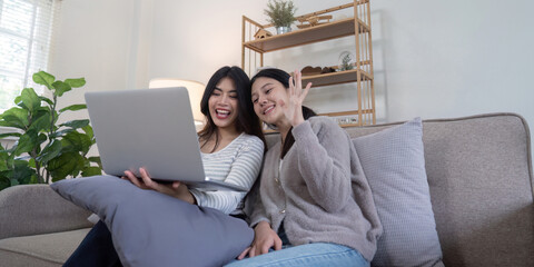 Happy Lesbian Couple Enjoying a Video Call Together on a Cozy Sofa in a Modern Living Room