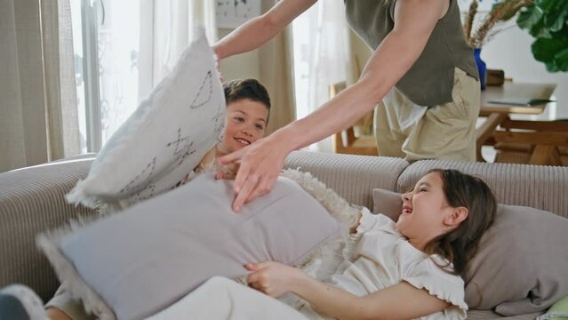 Excited siblings playing pillows sofa closeup. Mother calming naughty children