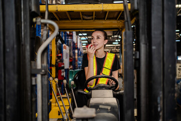 A woman in a yellow vest is driving a forklift. She is eating an apple while driving