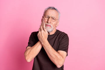 Portrait of suffering man with beard dressed t-shirt in glasses hold both hands on cheek have teeth ache isolated on pink color background