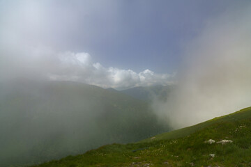  A panorama of a grass-covered hill with mountains behind and clouds above