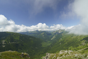  A valley viewed with mountains distantly, clouds in the sky above, and clouds in the foreground