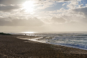 A beach with cloudy sky, sun shining through clouds, water, sky, beach..