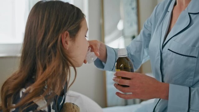 Woman giving mixture daughter at white bedroom closeup. Kid taking medicine