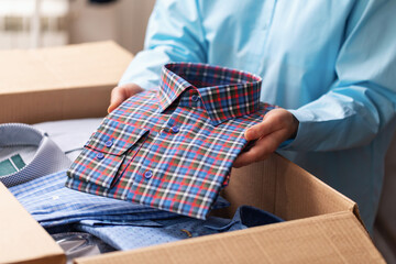 Woman putting folded new shirts into a box to send to marketplace, concept on small business theme