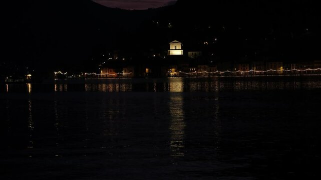 Veduta al tramonto di Peshiera maraglio dal porticciolo di Sulzano sul lago d'Iseo, traghetto con luci notturne arriva al porticciolo di Peshiera Maraglio