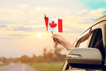 Waving the Canada flag against the sunrise or sunset from a car driving along a country road....