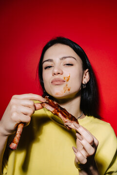 Woman eating ribs with sauce on face against red background