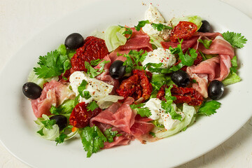 salad with dried tomatoes, prosciutto, soft cheese, olives, homemade, top view,
