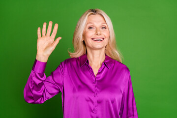 Photo portrait of nice senior female wave hand hello wear trendy violet satin outfit isolated on green color background © deagreez