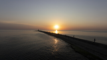 Fototapeta premium The sun sets over the water; people stand at pier's edge, watching it descend