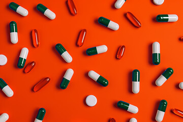 Scattered Green and White Capsules with Red Softgels on Vibrant Orange Background