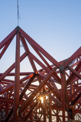 Detail of red metal beams and a blue crane in a modern construction against a clear blue sky.