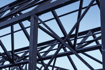 Detail of dark metal beams and a blue crane in a modern construction against a dark blue sky.