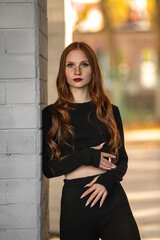 Portrait of a young beautiful red-haired girl in dark clothes outdoors.