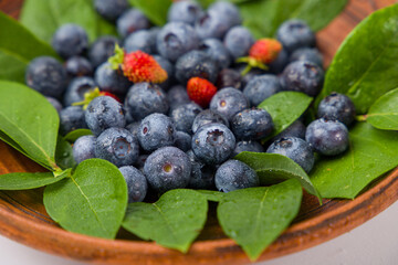 Fresh blueberries in a wooden bowl with green leaves
