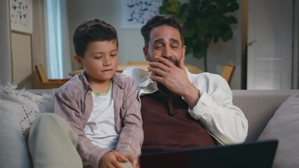 Dad son viewers laughing looking amusing film on laptop at cozy sofa closeup