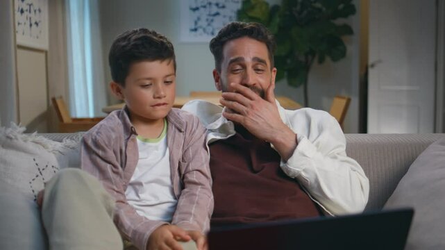 Dad son viewers laughing looking amusing film on laptop at cozy sofa closeup