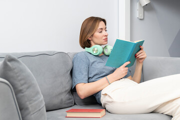 Attractive girl in headphones reading book at home. Audiobook and home education concept	