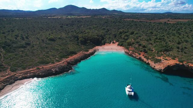 4K Aerial Drone video of the most incredible turquoise blue water color with a unique rocky cliff formation and boats anchored in on a beautiful summer sunny day, Cala Varques secluded beach, Mallorca