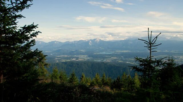 Timelapse moving backward in the valley of Villach in Austrian Alps with a pine forest and clouds