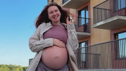 Young happy pregnant woman owner of new flat outdoors showing keys 