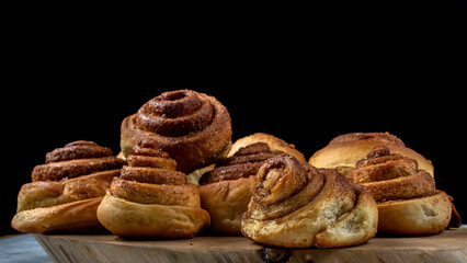 Freshly baked cinnamon rolls on a wooden board against a dark background.