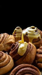 Close-up of cinnamon rolls with a big drop of creamy icing on a dark background.