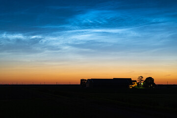 Fototapeta premium Scenic view of noctilucent clouds or NLC above a farm during the period of the shortest nights in June