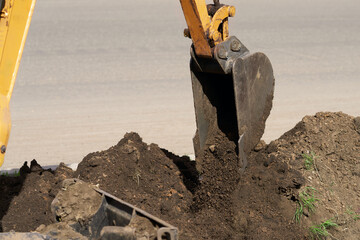 Fragment of a miniature crawler excavator digging a trench on a highway median strip.